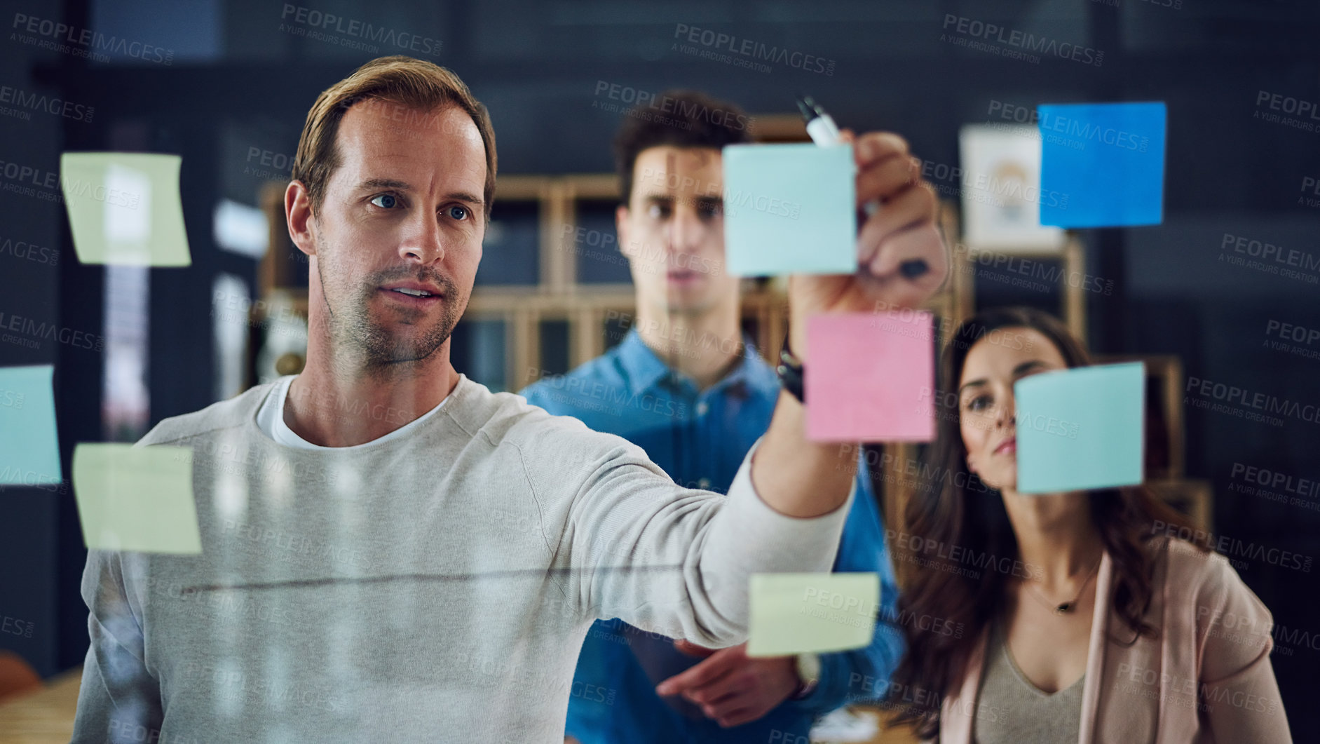 Buy stock photo Cropped shot of a group of young designers brainstorming with notes on a glass wall in an office