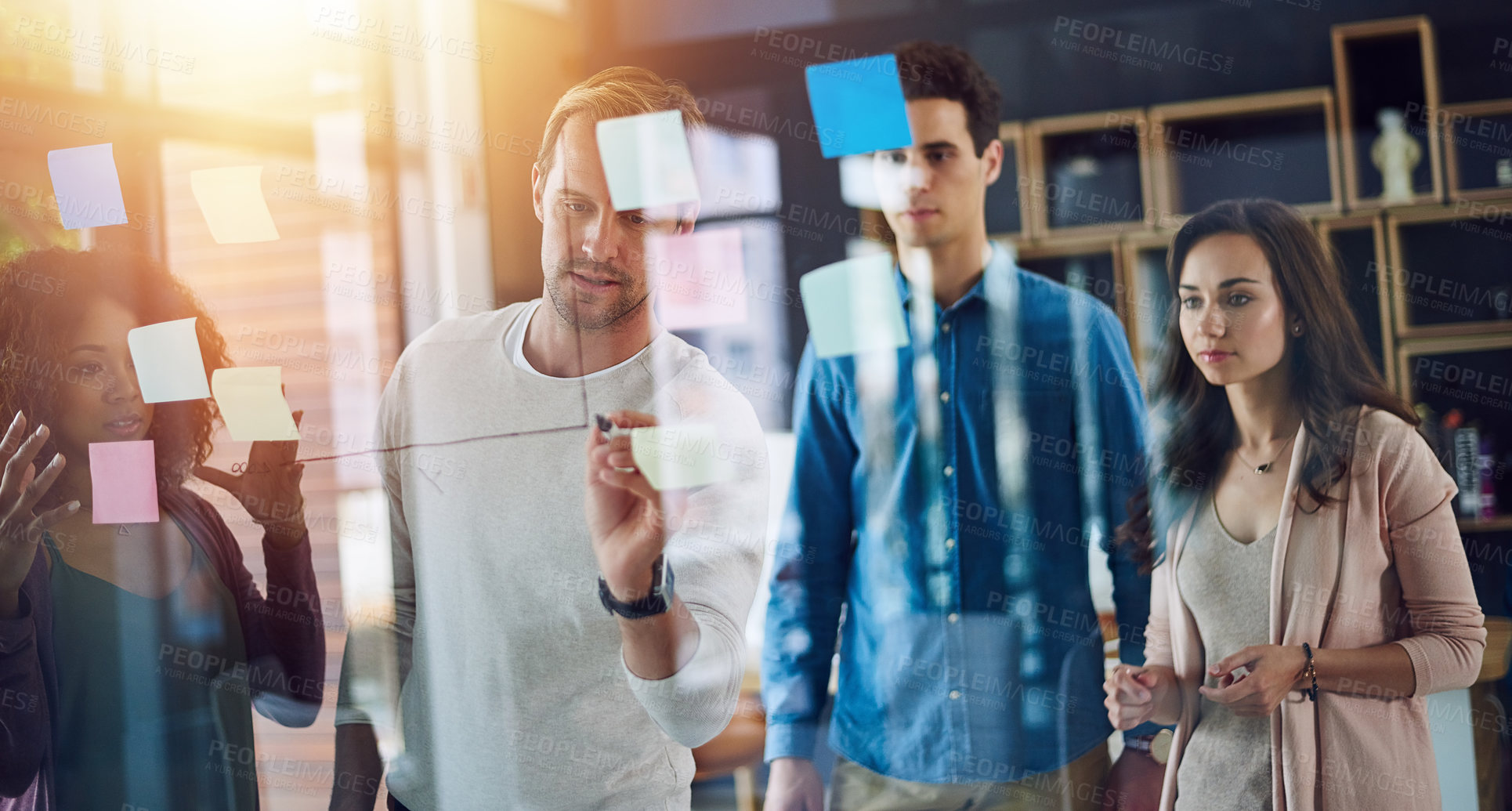 Buy stock photo Cropped shot of a group of young designers brainstorming with notes on a glass wall in an office