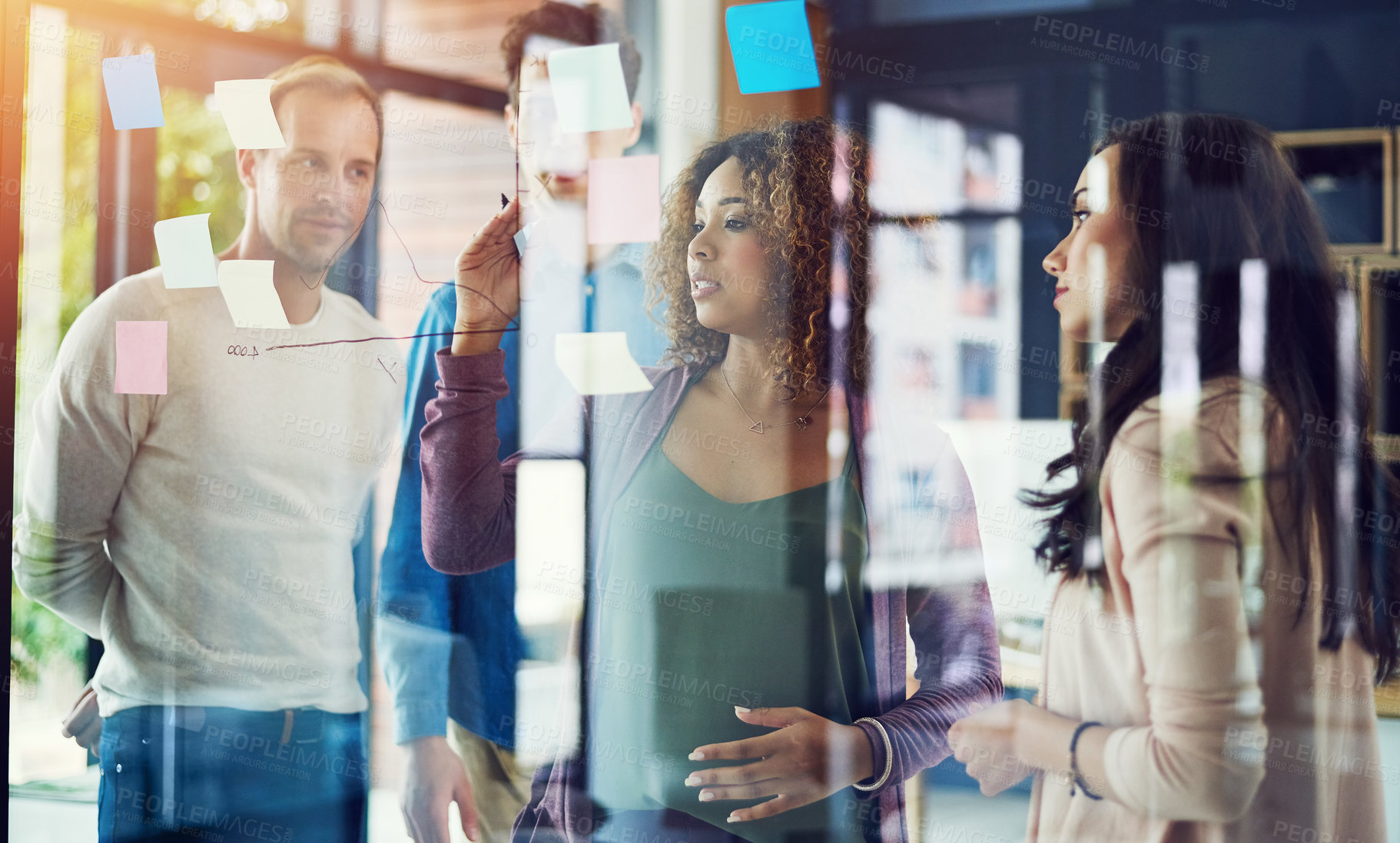 Buy stock photo Cropped shot of a group of young designers brainstorming with notes on a glass wall in an office