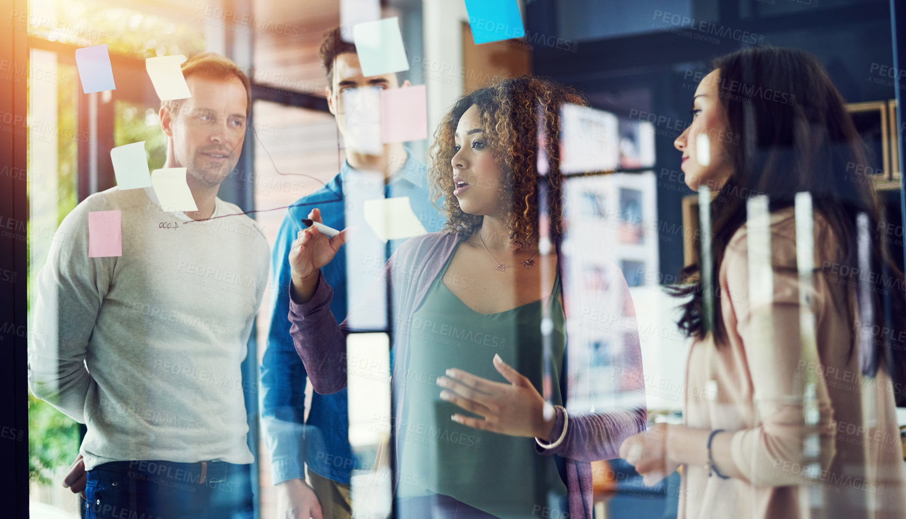 Buy stock photo Cropped shot of a group of young designers brainstorming with notes on a glass wall in an office