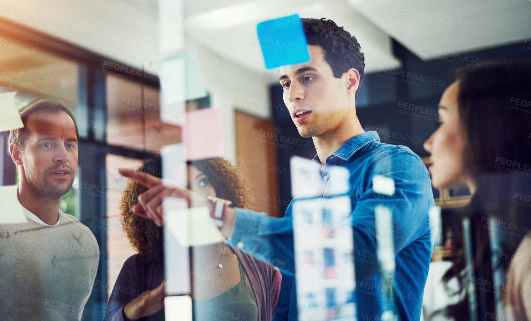 Buy stock photo Cropped shot of a group of young designers brainstorming with notes on a glass wall in an office