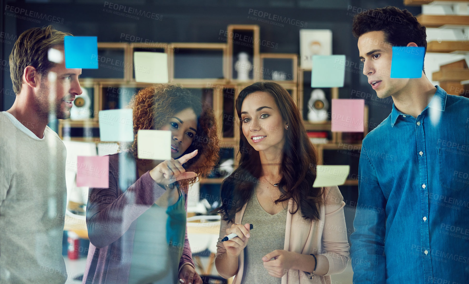 Buy stock photo Cropped shot of a group of young designers brainstorming with notes on a glass wall in an office