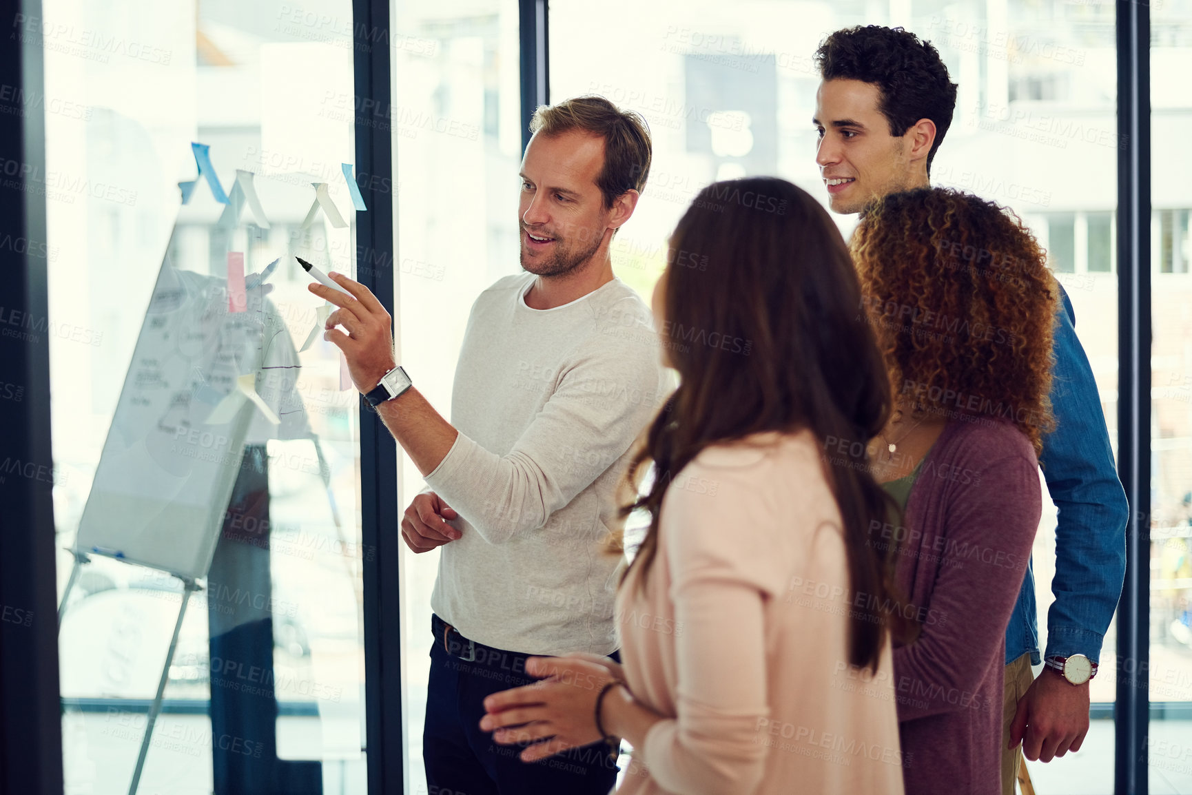 Buy stock photo Cropped shot of a group of young designers brainstorming with notes on a glass wall in an office
