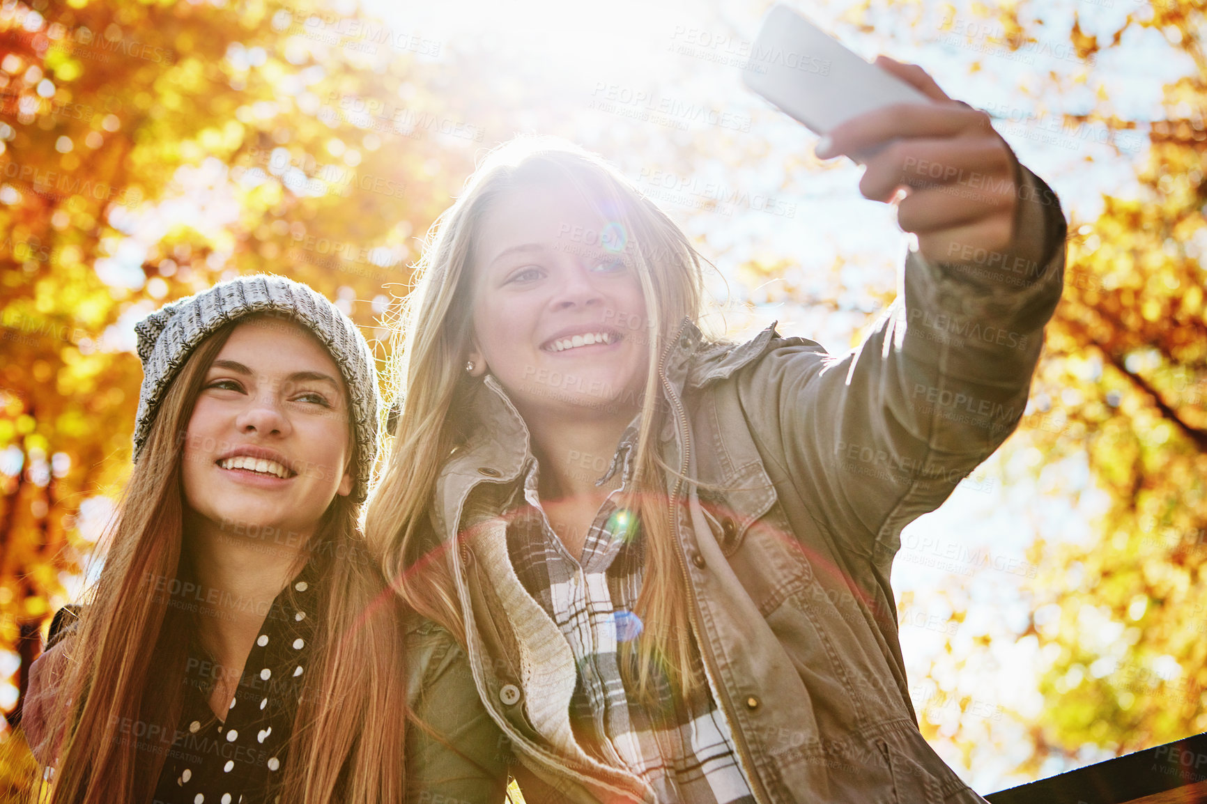 Buy stock photo Shot of two young friends taking selfies together on a mobile phone while out in the park