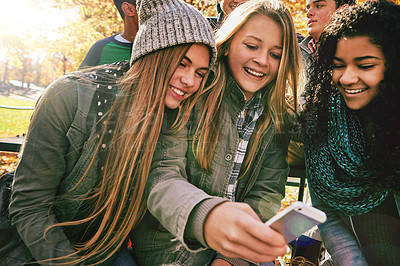 Buy stock photo Shot of a group of young friends using a mobile phone together while out in the park