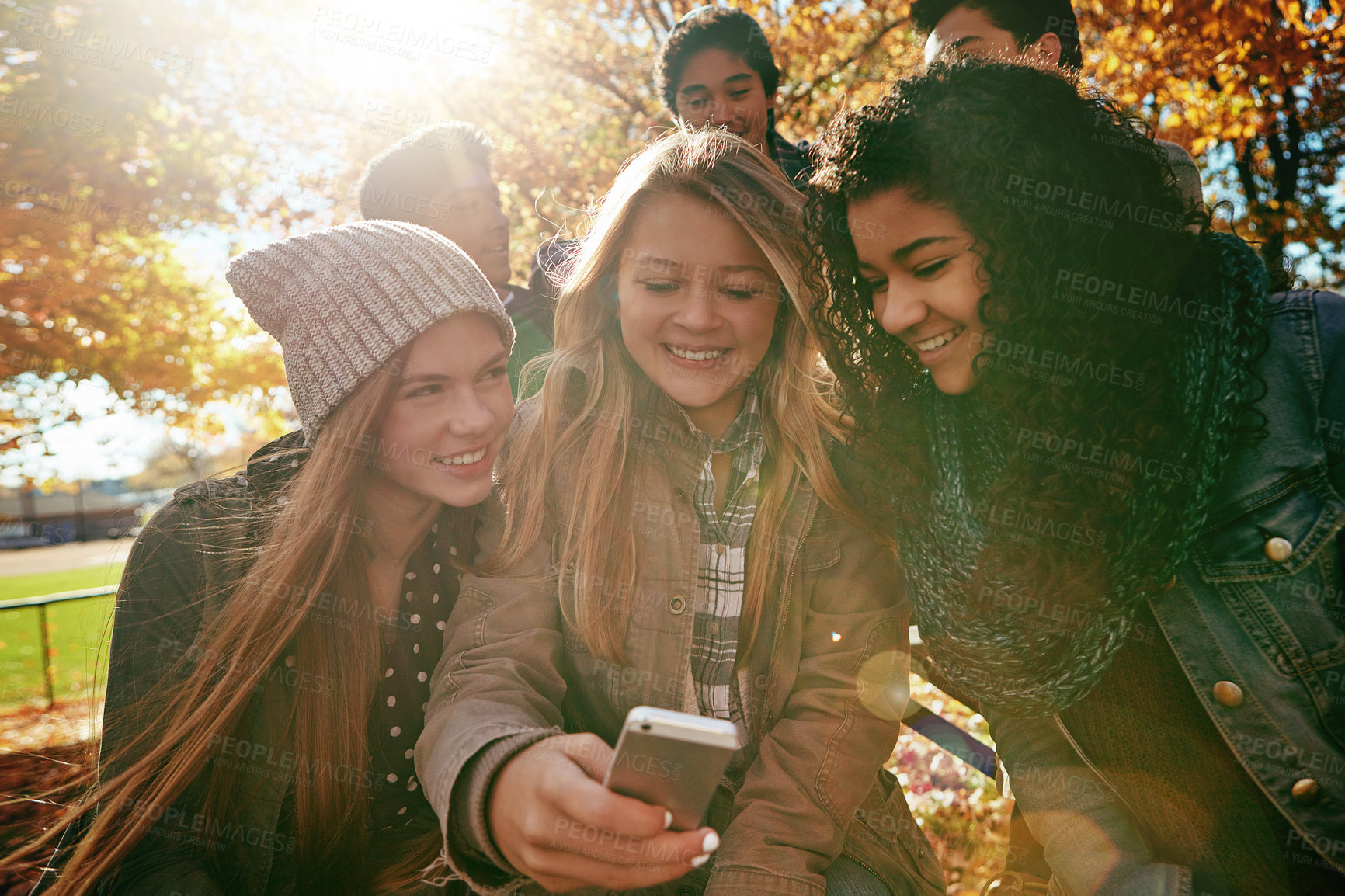 Buy stock photo Teen, friends and smile in park with phone, text message joke and social media for bonding together. Happy, kids or people chill outdoor with tech, online chat and internet humor for weekend hangout.