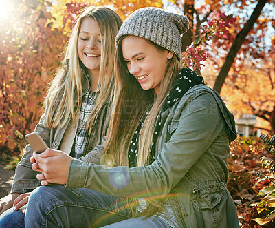 Buy stock photo Shot of two young friends using a mobile phone together while out in the park