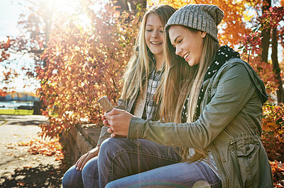 Buy stock photo Shot of two young friends using a mobile phone together while out in the park