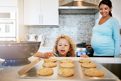 Buy stock photo Cropped shot of a little boy reaching out for a freshly baked cookie with his mother watching in the background