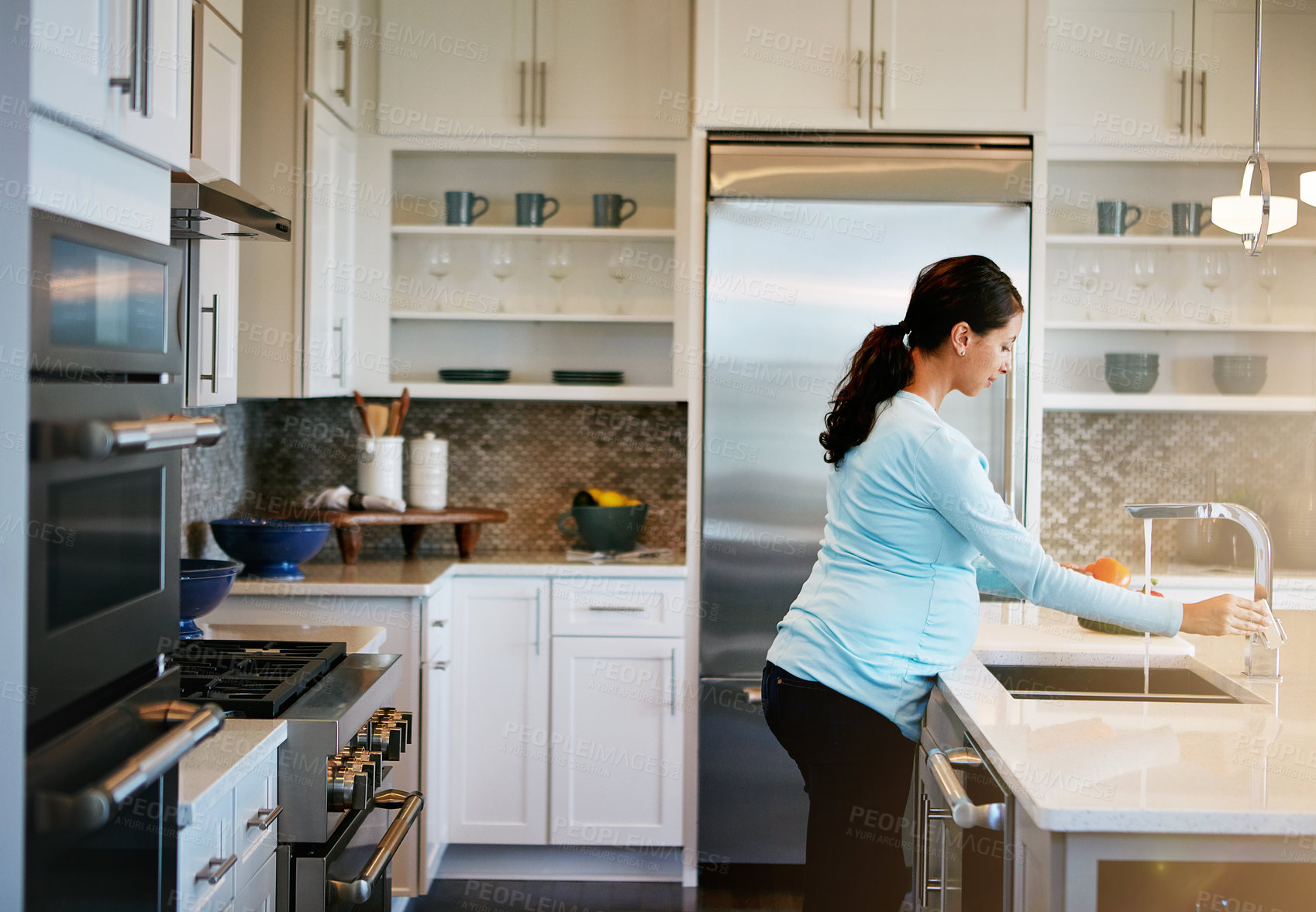 Buy stock photo Cropped shot of a pregnant woman washing vegetables in the kitchen sink