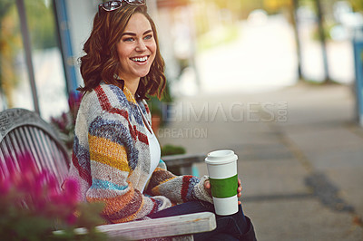 Buy stock photo Shot of a happy young woman drinking coffee while relaxing on a bench downtown