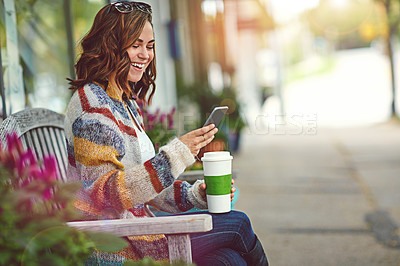 Buy stock photo Shot of a happy young woman using her cellphone while relaxing on a bench downtown