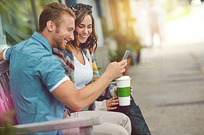 Buy stock photo Shot of a happy young couple using a smartphone together while spending the day downtown
