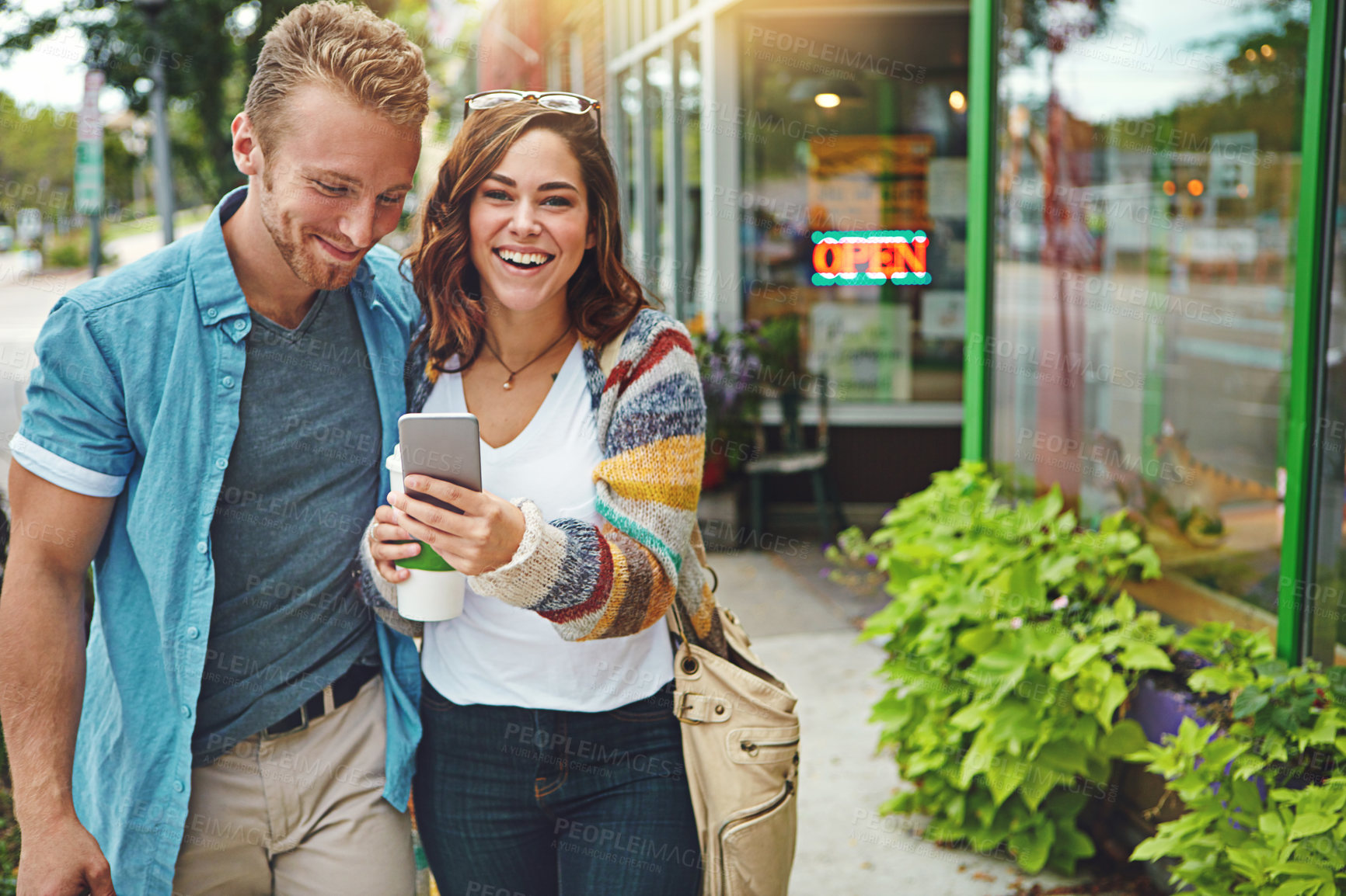 Buy stock photo Shot of a happy young couple using a smartphone together while spending the day downtown