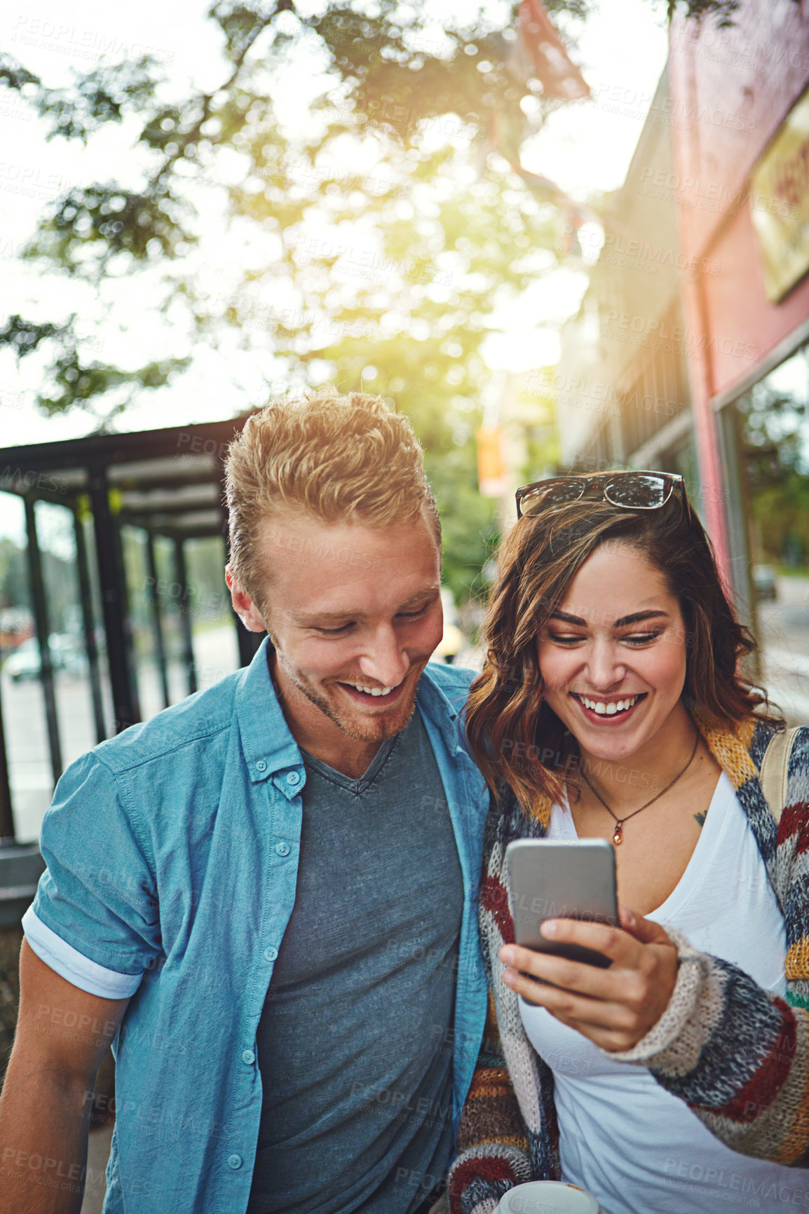 Buy stock photo Shot of a happy young couple using a smartphone together while spending the day downtown