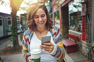 Buy stock photo Shot of a happy young woman using her cellphone while taking a walk downtown