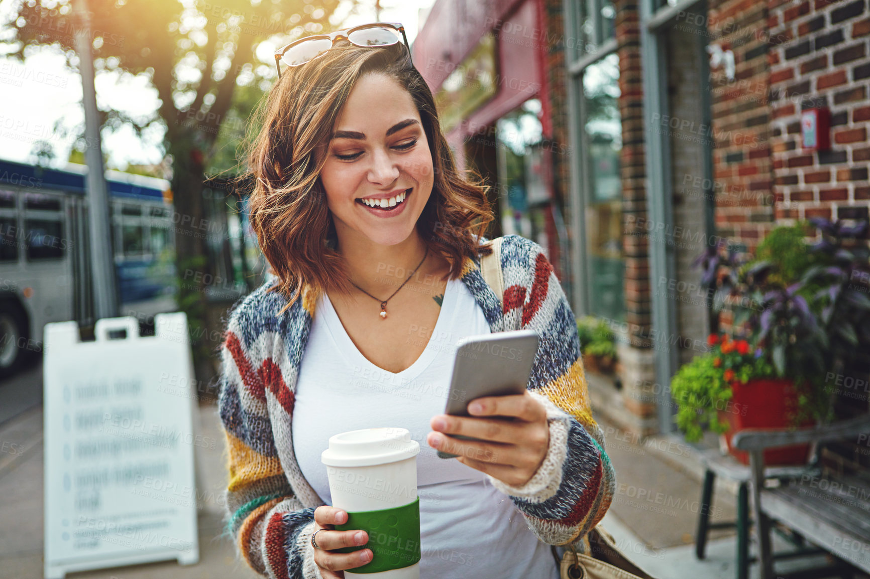 Buy stock photo Shot of a happy young woman using her cellphone while taking a walk downtown