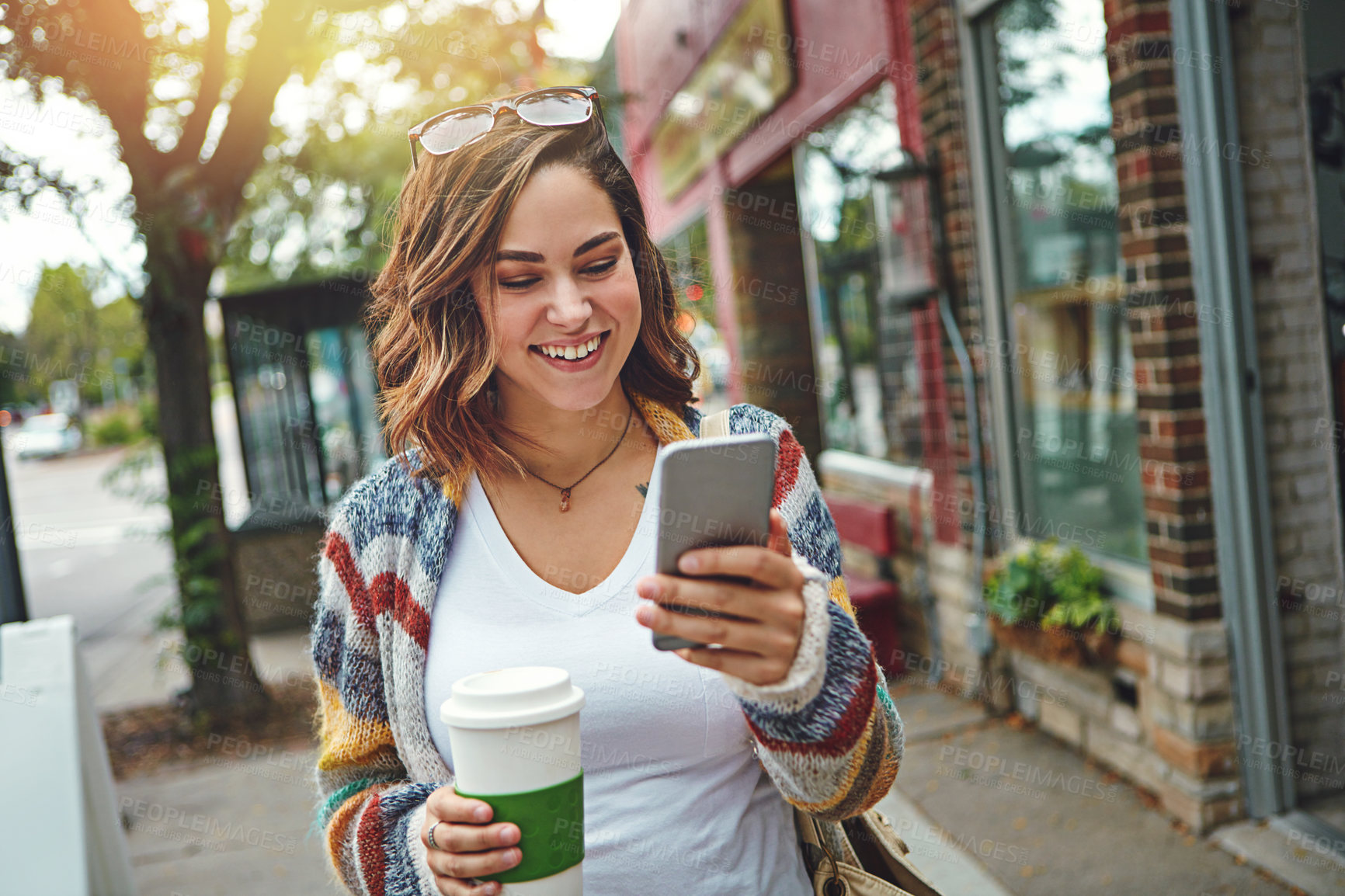 Buy stock photo Shot of a happy young woman using her cellphone while taking a walk downtown