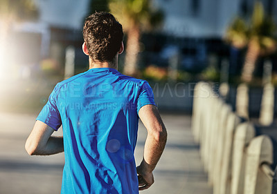 Buy stock photo Rearview shot of a sporty young man out for a run