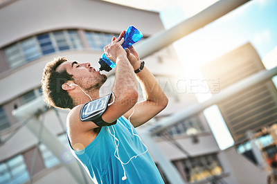Buy stock photo Low angle shot of a handsome young man taking a drink while working out in the city