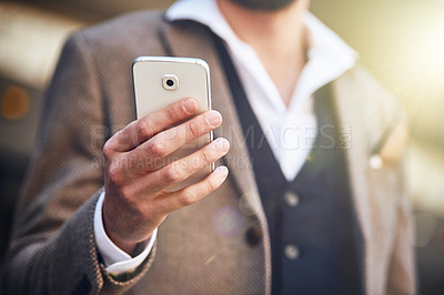 Buy stock photo Cropped shot of a young man using his cellphone while standing outside