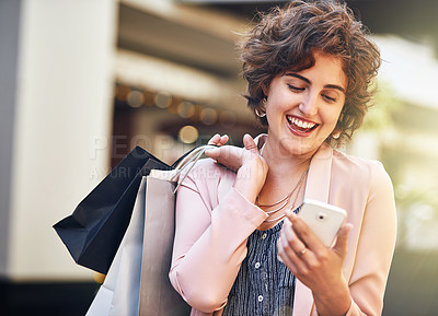 Buy stock photo Shot of a young woman carrying shopping bags and reading a text on her phone