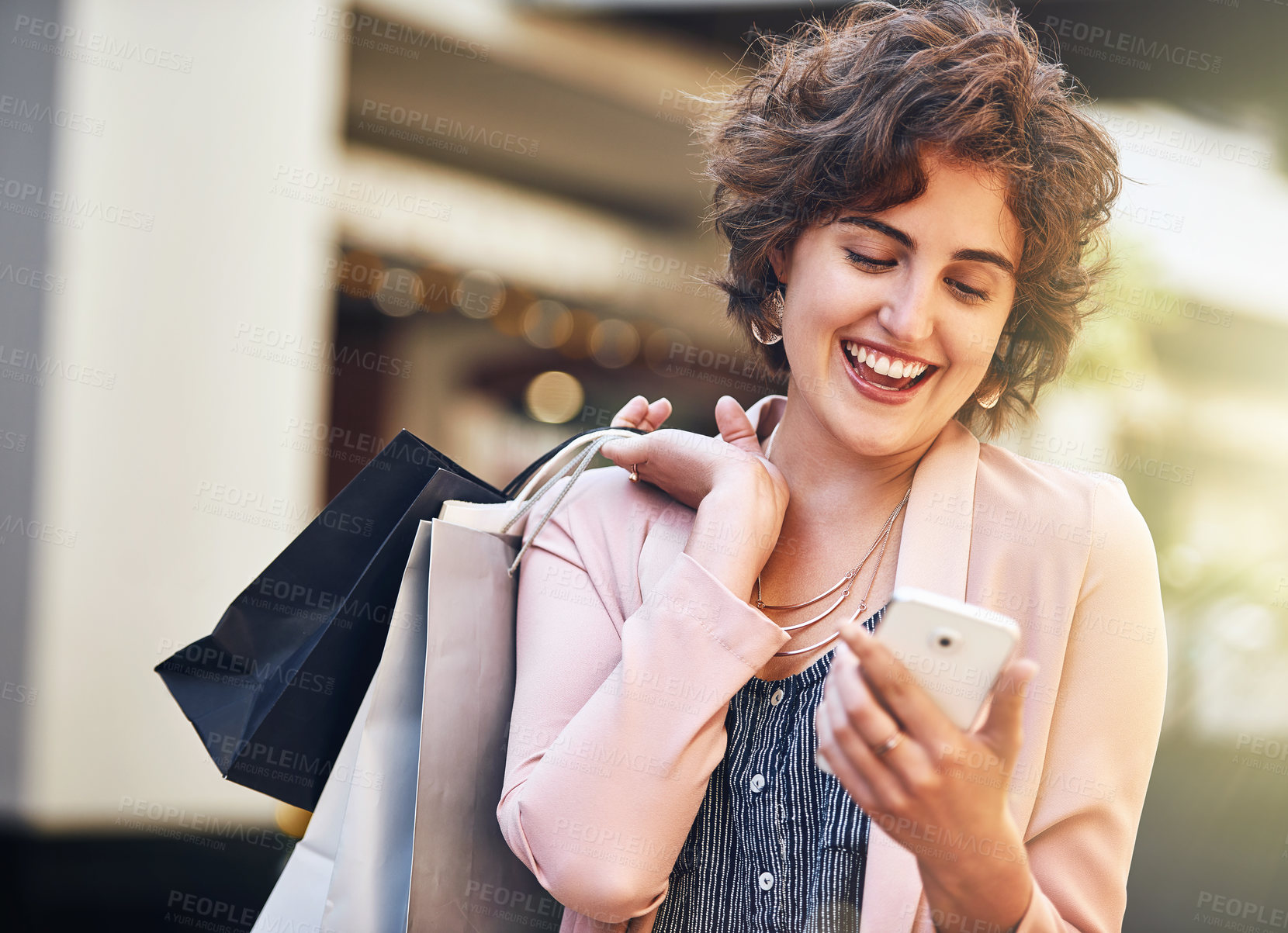 Buy stock photo Shot of a young woman carrying shopping bags and reading a text on her phone