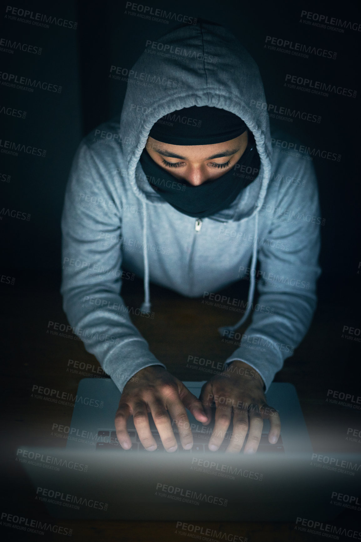 Buy stock photo High angle shot of a man in a hoodie and mask hacking a computer network