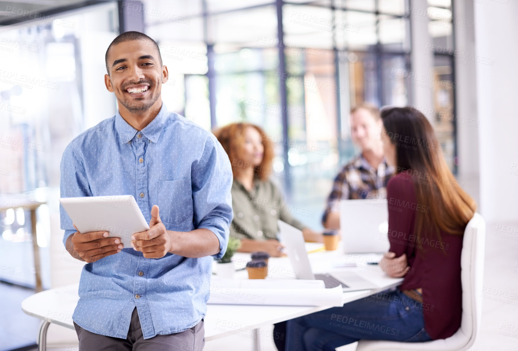 Buy stock photo Portrait of a young designer working on a digital tablet with his colleagues in the background