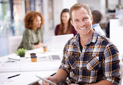 Buy stock photo Portrait of a young designer working on a digital tablet with his colleagues in the background