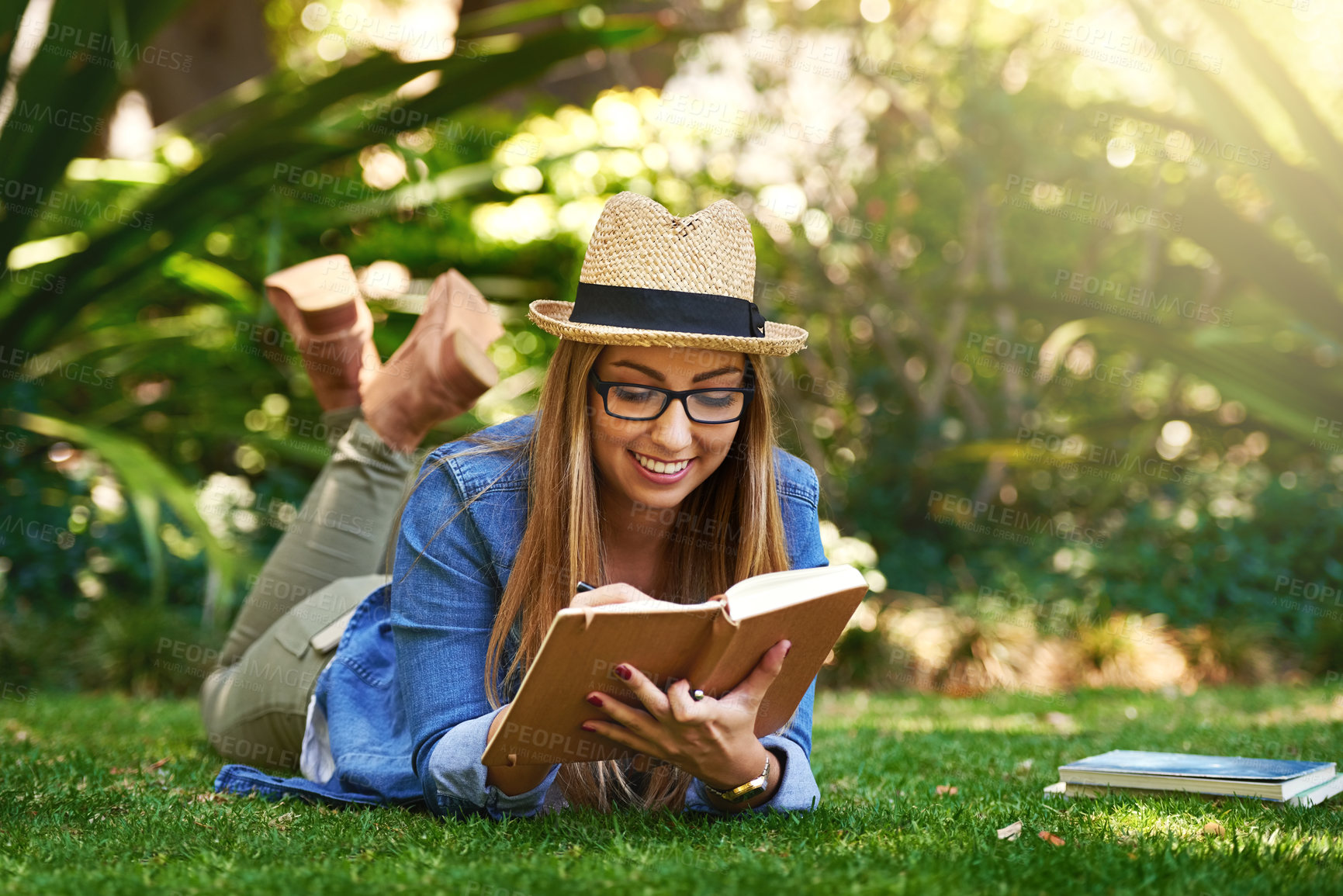 Buy stock photo Park, girl and lying with book for reading to learn, knowledge and entertainment with smile outdoor. Nature, female author and novel of horror, romance and crime literature for language improvement