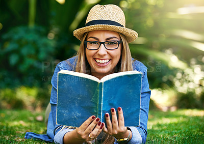 Buy stock photo Portrait of an attractive young woman reading a book while lying outside on the grass