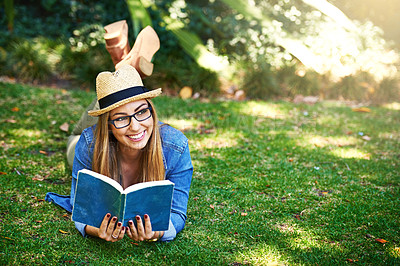 Buy stock photo Shot of an attractive young woman reading a book while lying outside on the grass