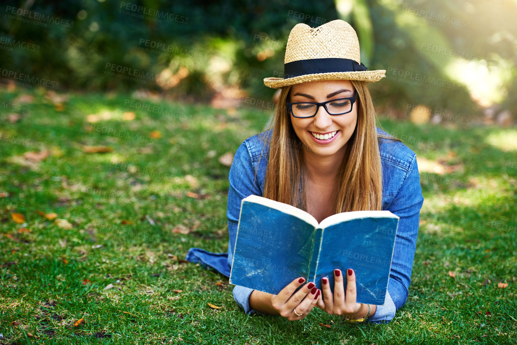 Buy stock photo Shot of an attractive young woman reading a book while lying outside on the grass