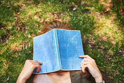 Buy stock photo Shot of an unrecognizable woman reading a book while lying outside on the grass