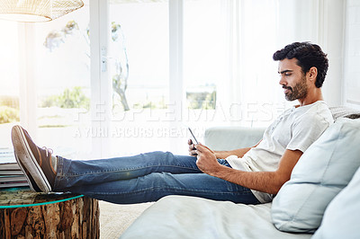 Buy stock photo Shot of a man using a digital tablet and relaxing on the sofa at home