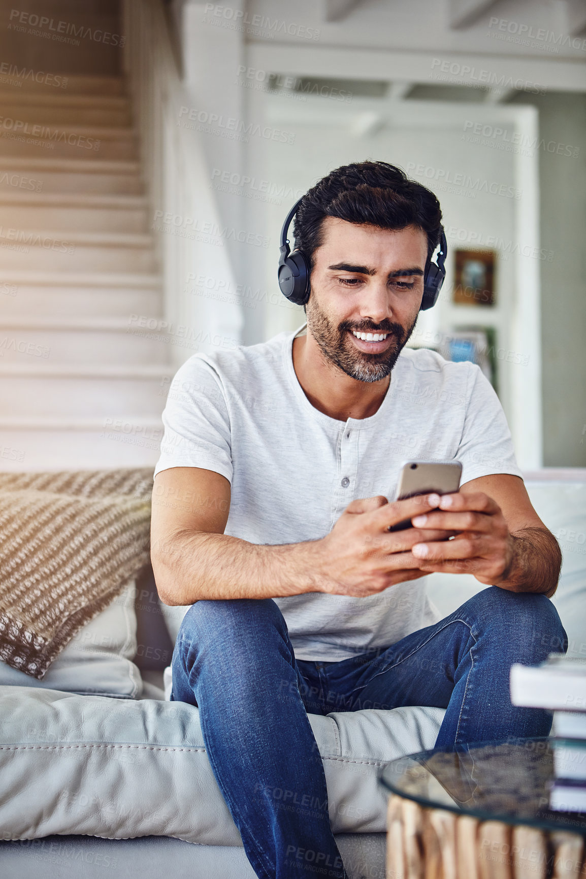 Buy stock photo Man, phone and happy with headphones on sofa for music, radio and streaming podcast in living room with relax. Person, smartphone and mobile app for listening to audio, sound and subscription in home