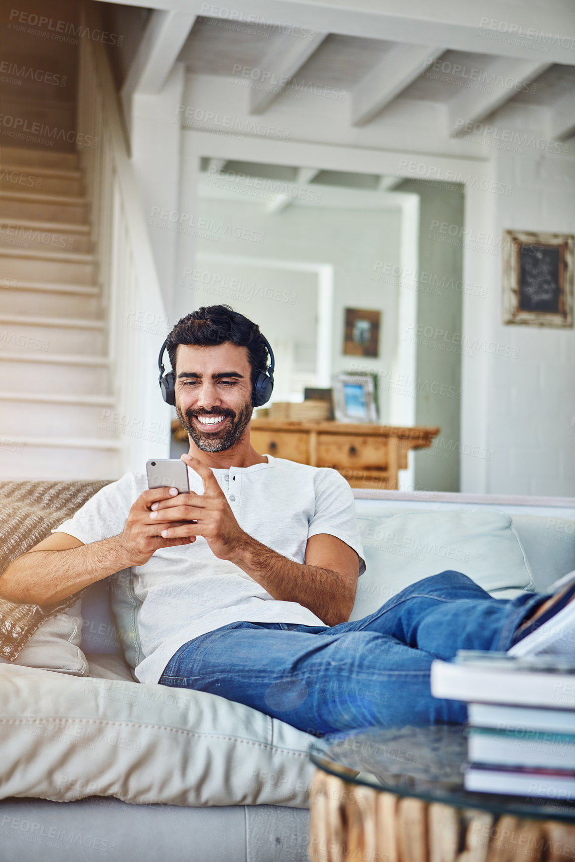 Buy stock photo Man, phone and happy with headphones on sofa for music, radio and streaming podcast in living room with relax. Person, smartphone and mobile app for listening to audio, sound and subscription in home