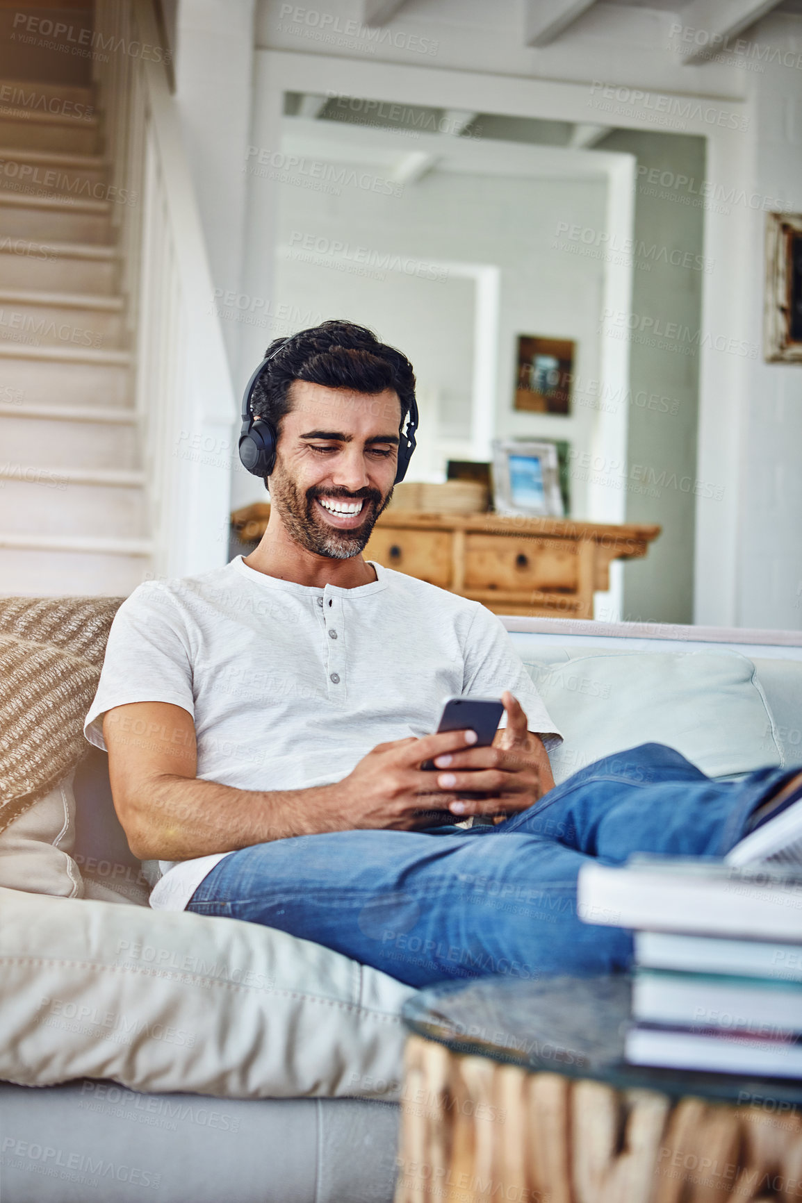 Buy stock photo Man, headphones and laughing for phone on couch with funny social media post and comedy movie on mobile app. Person, smartphone and happy with relax for listening to audio, sound and track on sofa