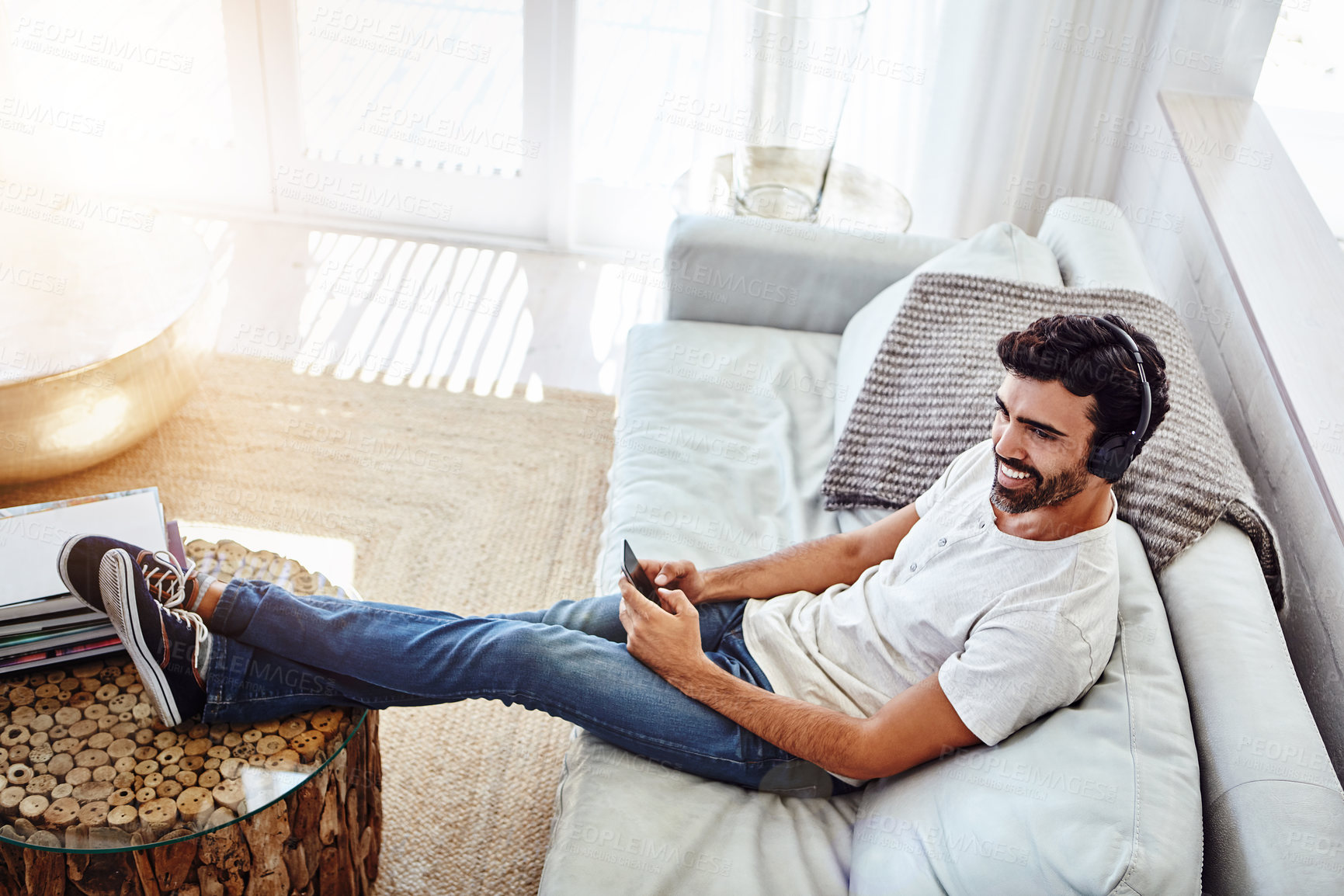 Buy stock photo Thinking, man and cellphone with headphones on sofa to listen to music, radio and network at home. Lounge, male chatter and mobile app for streaming podcast, online games or social media to relax