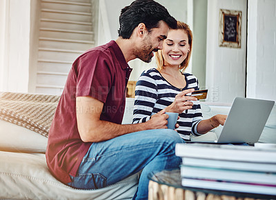 Buy stock photo Shot of an affectionate young couple shopping online while sitting on their sofa at home