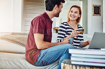 Buy stock photo Shot of an affectionate young couple shopping online while sitting on their sofa at home