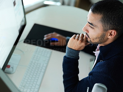 Buy stock photo Shot of a focused young man sitting at a desk working on a computer with dual monitors