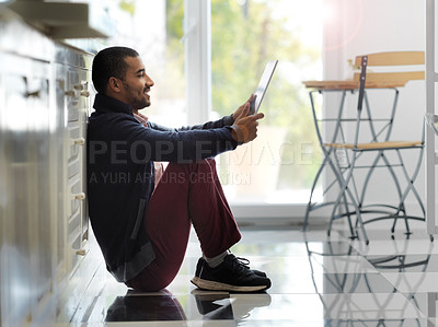 Buy stock photo Shot of a smiling young man sitting on his kitchen floor using a digital tablet