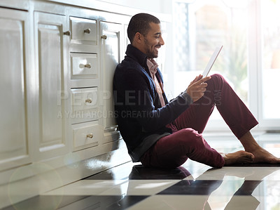 Buy stock photo Shot of a smiling young man sitting on his kitchen floor using a digital tablet
