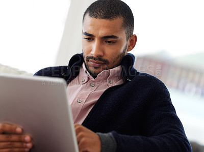Buy stock photo Shot of a focused young man working at home on a digital tablet