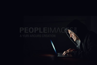 Buy stock photo Shot of a hooded computer hacker using a laptop in the dark