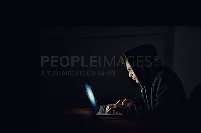 Buy stock photo Shot of a hooded computer hacker using a laptop in the dark
