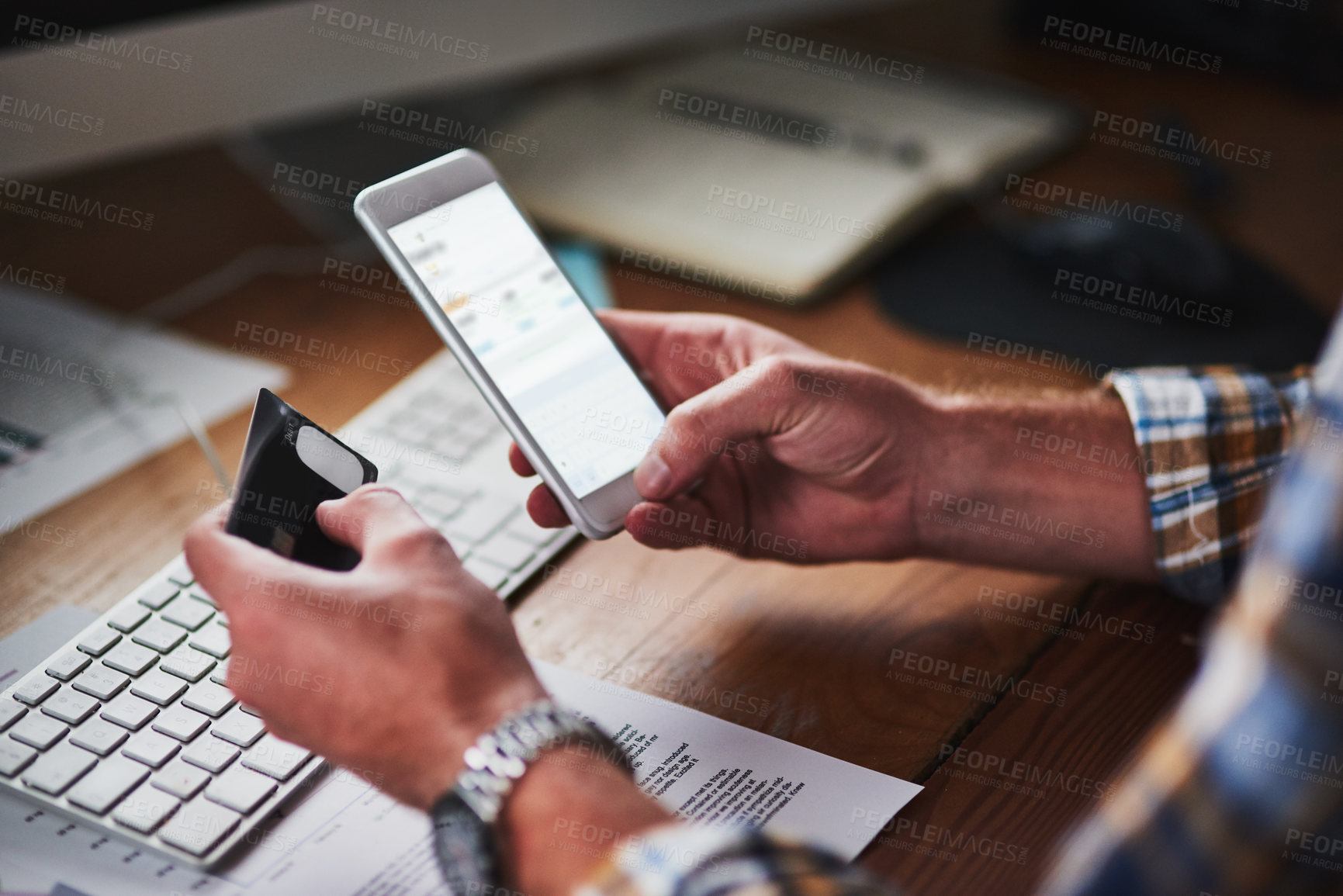 Buy stock photo Shot of an unidentifiable programmer holding his credit card while using his smartphone