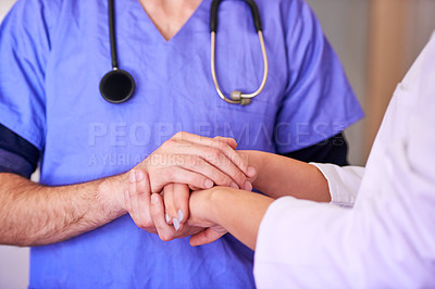 Buy stock photo Shot of an unidentifiable young doctor holding hands with a nurse in her office